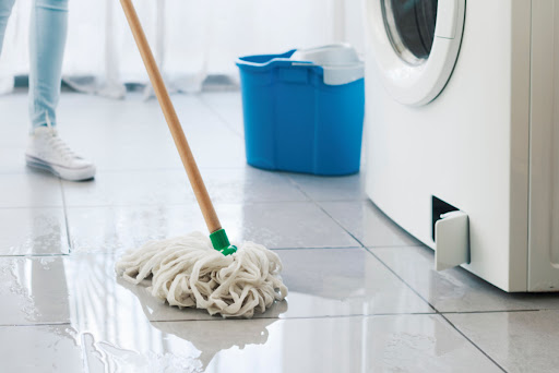 A person using a mop near a washing machine. There is water on the floor.