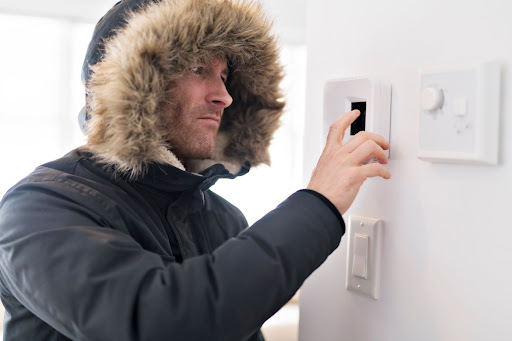 A man wearing a winter jacket adjusting the thermostat in a home.