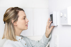 A woman adjusting a thermostat.