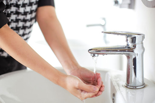 Homeowner washing hands with hot water from bathroom tap.