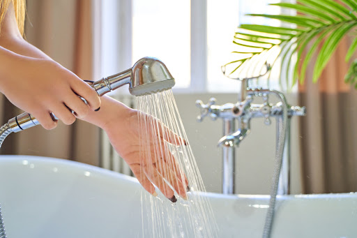 A woman feeling the water flowing out of a showerhead.
