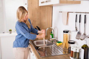Woman plunging slow draining sink in her kitchen as part of monthly drain cleaning maintenance.