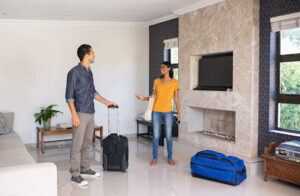 A man and woman smiling with suitcases in a house.