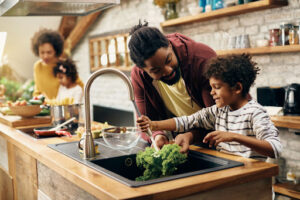 A father and son washing vegetables in a kitchen sink.