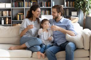 Family of 3 sitting on the couch each holding a glass of tap water to drink