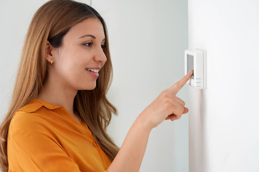 A woman adjusting the settings on a thermostat.