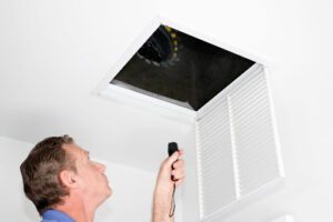 A man shining a flashlight into a home's ductwork.