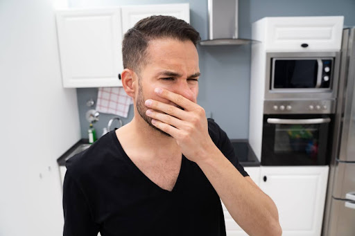 A man covering his nose due to a bad smell in a kitchen.